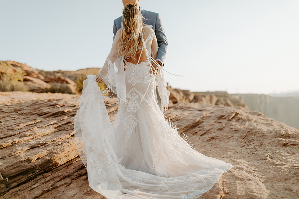  bride and groom dancing on the cliffside, bride in an ivory lace gown with bellowing sleeves and a boho design.  The groom is in a light blue suit with matching vest and no tie