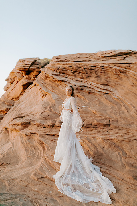  bride in an ivory lace gown with bellowing sleeves and a boho design resting on the side of the cliff 