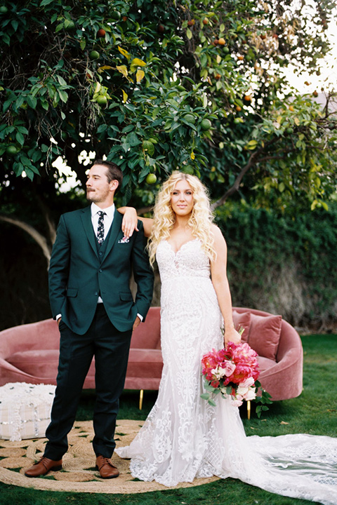  bride in a vintage bohemian gown with beaded details and cape, groom in a green suit with a floral tie standing by the couch