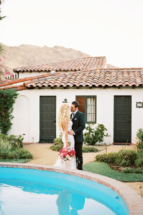  bride in a vintage bohemian gown with beaded details and cape, groom in a green suit with a floral tie by the pool