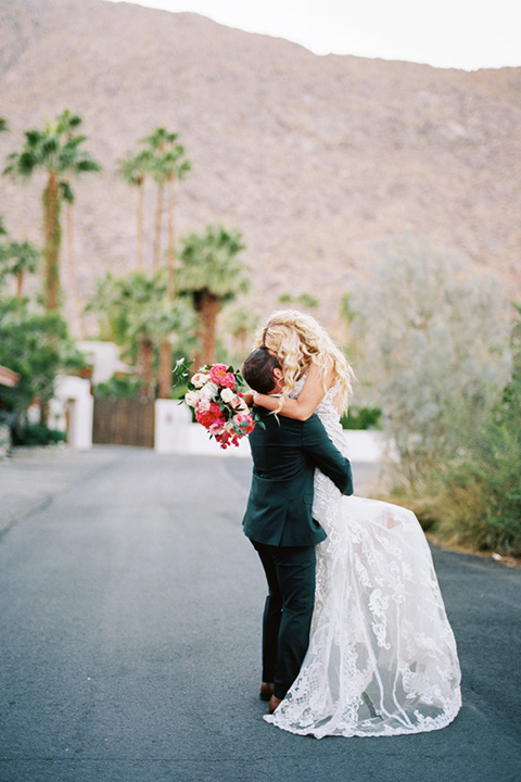  bride in a vintage bohemian gown with beaded details and cape, groom in a green suit with a floral tie by the pool