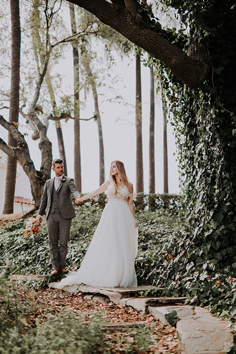  bride in a bohemian lace gown with a tulle skirt, lace boots, and headpiece and the groom in a café brown suit with an ivory tie, with a geometric arch