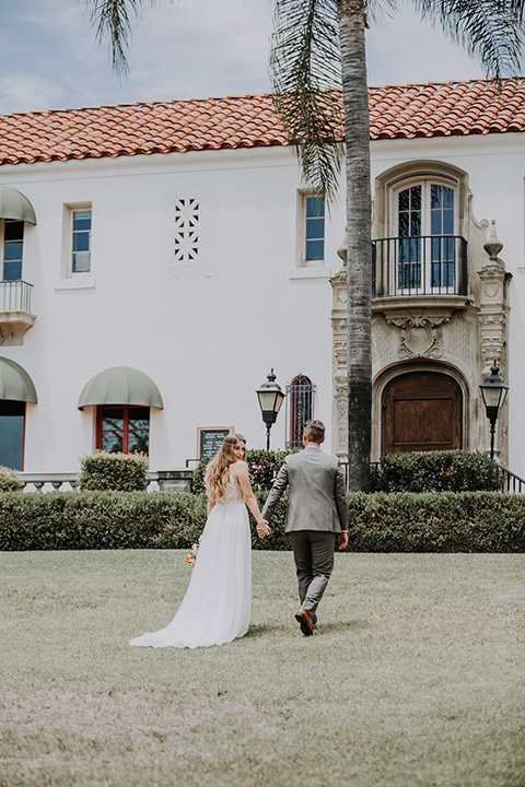  bride in a bohemian lace gown with a tulle skirt, lace boots, and headpiece and the groom in a café brown suit with an ivory tie, with a geometric arch 