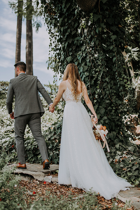  bride in a bohemian lace gown with a tulle skirt, lace boots, and headpiece and the groom in a café brown suit with an ivory tie, with a geometric arch 