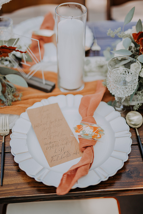  white plates with burnt orange linens and gold flatware