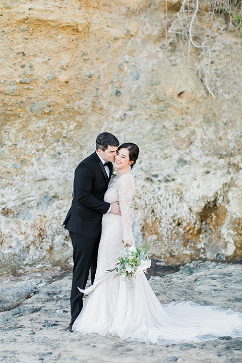  bride in a flowing gown with an illusion neckline and hair in a soft updo with a crystal pin detail and the groom in a black notch lapel suit with a black bow tie by the rock cliff