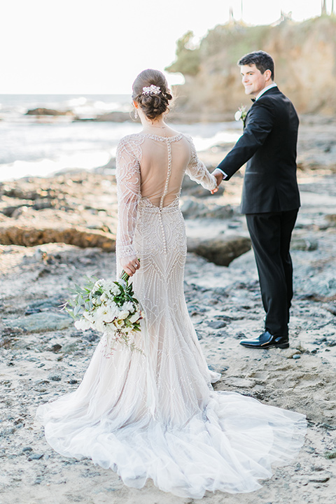 bride in a flowing gown with an illusion neckline and hair in a soft updo with a crystal pin detail and the groom in a black notch lapel tuxedo with a black bow tie kissing