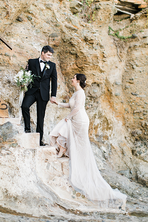  bride in a flowing gown with an illusion neckline and hair in a soft updo with a crystal pin detail and the groom in a black notch lapel suit with a black bow tie under veil 