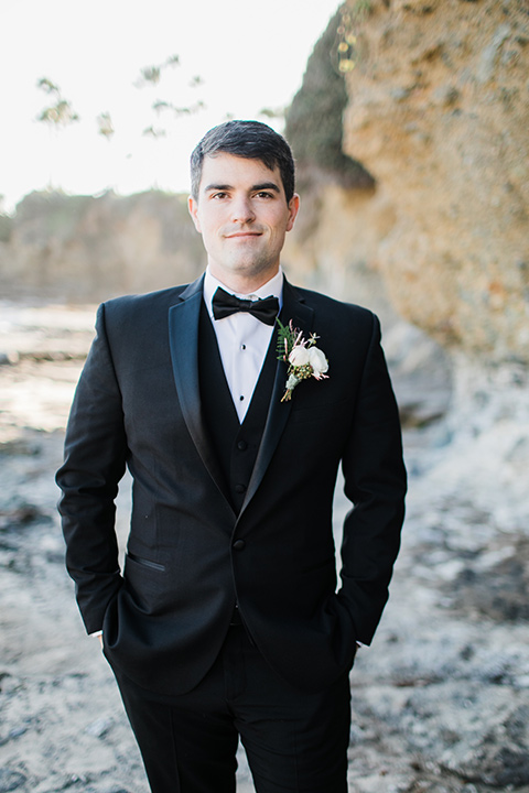  the groom in a black notch lapel suit with a black bow tie 