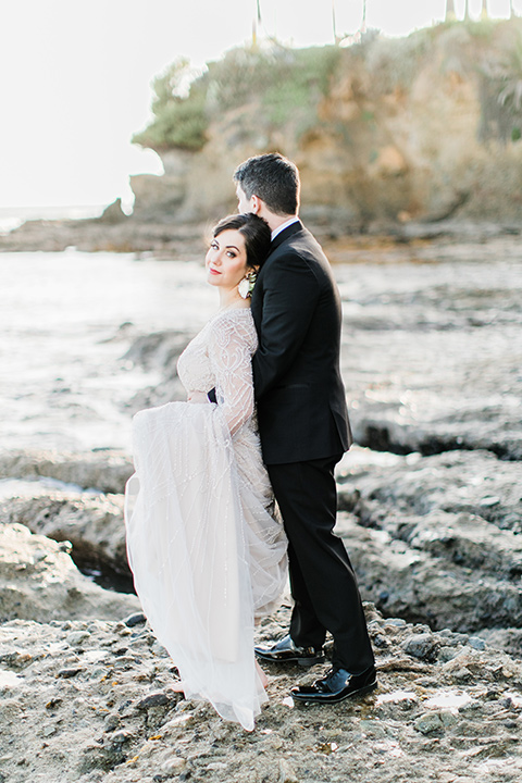  bride in a flowing gown with an illusion neckline and hair in a soft updo with a crystal pin detail and the groom in a black notch lapel suit with a black bow tie under veil 