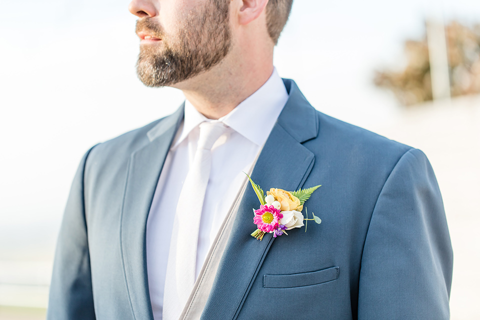  bride in a lace gown with thin straps and beaded bodice, the groom in a blue suit coat and tan pants with a white long tie 