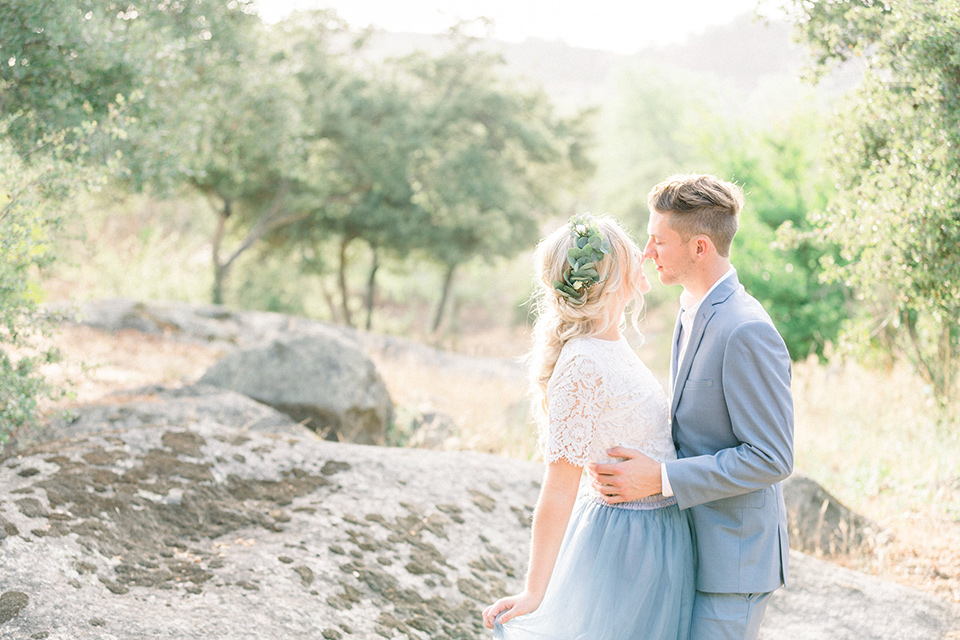 bride in a two-piece gown with a blue tulle skirt and white lace shirt and her hair in a loose French braid and floral crown groom in a light blue suit with no tie and brown shoes