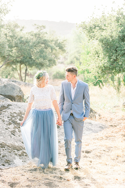 bride in a two-piece gown with a blue tulle skirt and white lace shirt and her hair in a loose French braid and floral crown groom in a light blue suit with no tie and brown shoes