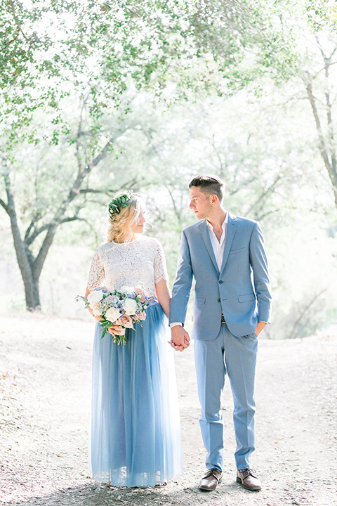 bride in a two-piece gown with a blue tulle skirt and white lace shirt and her hair in a loose French braid and floral crown groom in a light blue suit with no tie and brown shoes