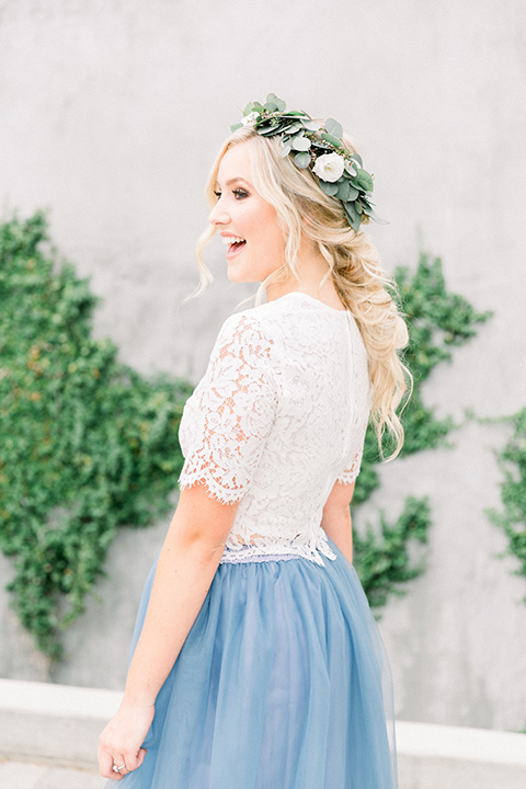  bride in a two-piece gown with a blue tulle skirt and white lace shirt and her hair in a loose French braid and floral crown 