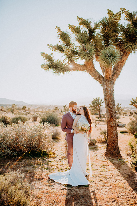  bride in a high neckline gown with lace details, groom in a rose pink suit with a bow tie 