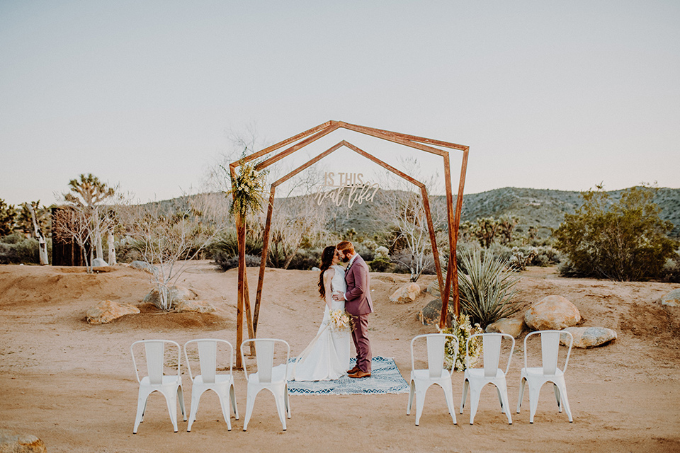  bride in a high neckline gown with lace details, groom in a rose pink suit with a bow tie 