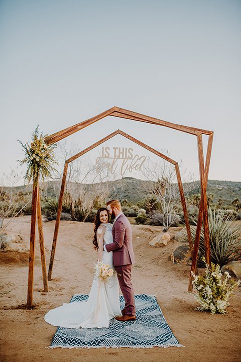  bride in a high neckline gown with lace details, groom in a rose pink suit with a bow tie 