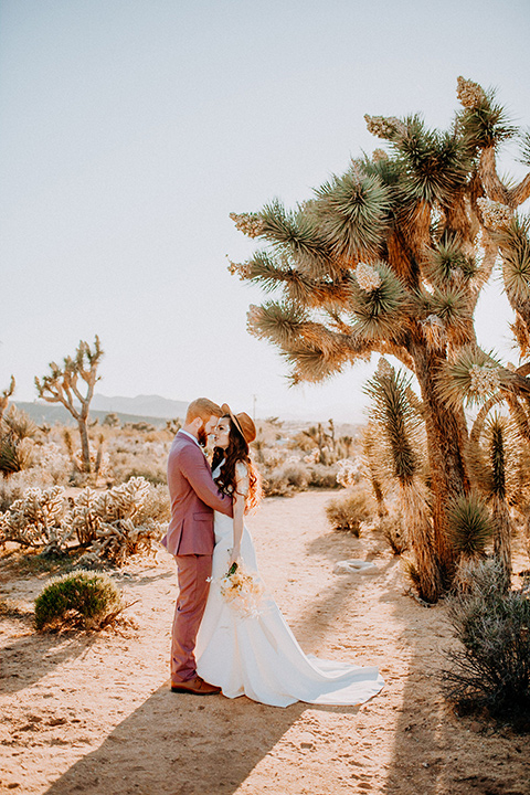  bride in a high neckline gown with lace details, groom in a rose pink suit with a bow tie