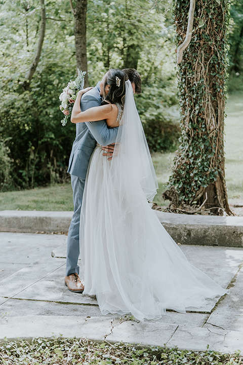  bride in a white ballgown with a high slit on the leg and v-neckline and groom in light blue suits with a long tie first look