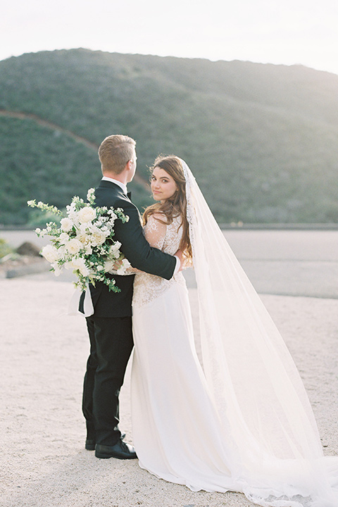  bride in a white lace ballgown with long sleeves and a v-neckline and the groom in a black tuxedo with a black bow tie and pocket square 