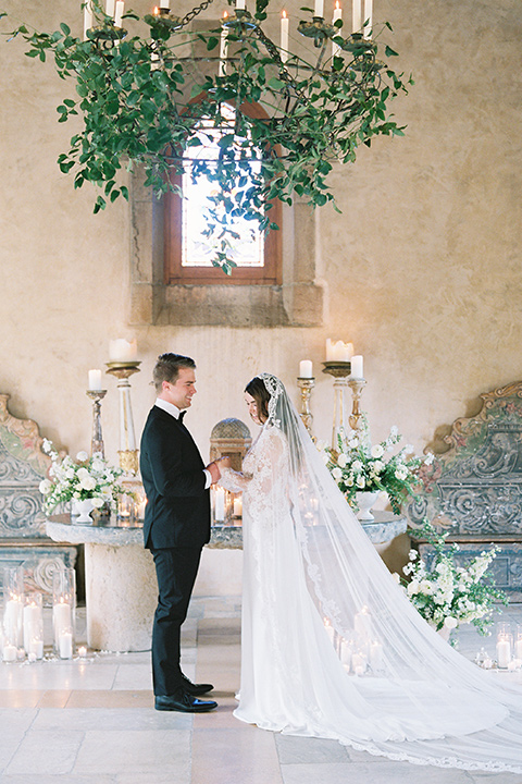  bride in a white lace ballgown with long sleeves and a v-neckline and the groom in a black tuxedo with a black bow tie and pocket square 