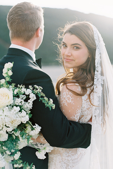  bride in a white lace ballgown with long sleeves and a v-neckline and the groom in a black tuxedo with a black bow tie and pocket square 