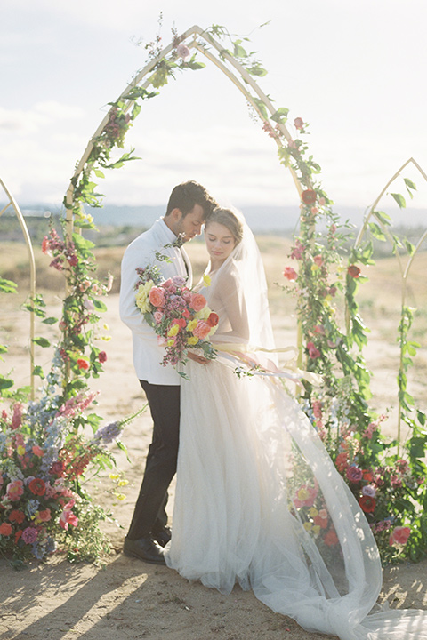  bride in a white flowing gown with a v neckline and the groom in a white dinner jacket and black pants 