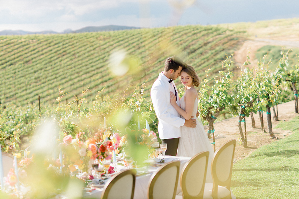  bride in a white flowing gown with a v neckline and the groom in a white dinner jacket and black pants 