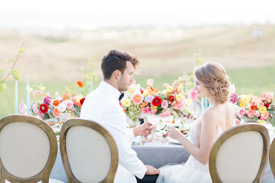  bride in a white flowing gown with a v neckline and the groom in a white dinner jacket and black pants 