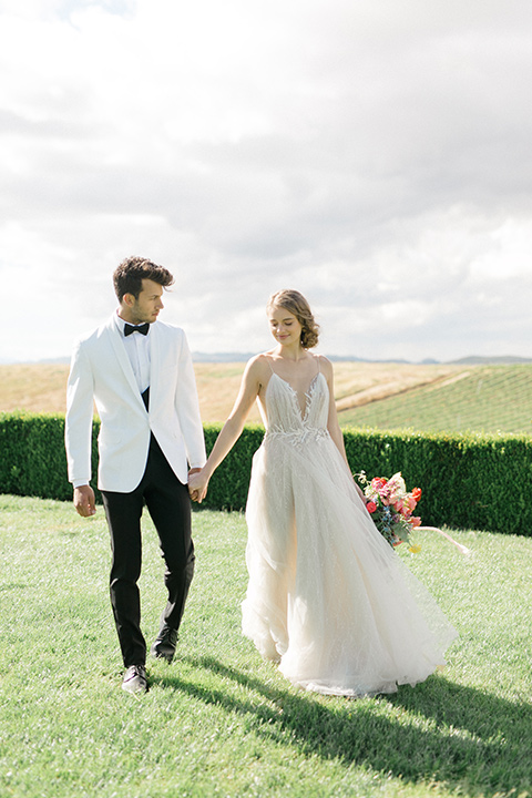  bride in a white flowing gown with a v neckline and the groom in a white dinner jacket and black pants 
