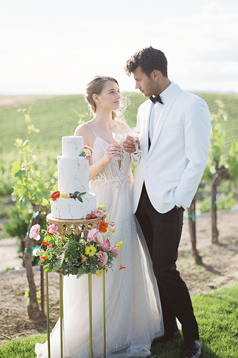  bride in a white flowing gown with a v neckline and the groom in a white dinner jacket and black pants 