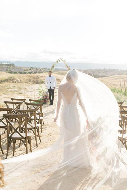  bride in a white flowing gown with a v neckline and the groom in a white dinner jacket and black pants 