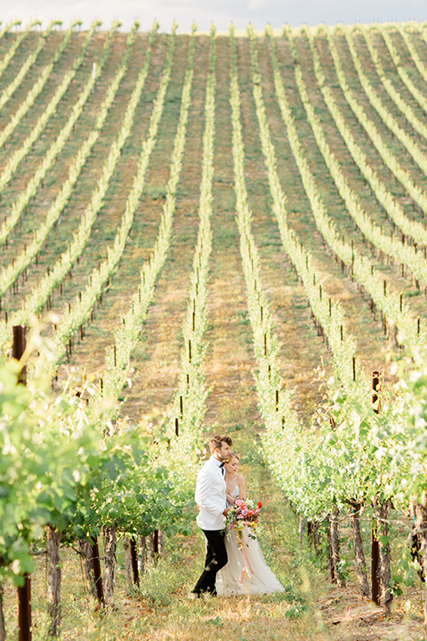  bride in a white flowing gown with a v neckline and the groom in a white dinner jacket and black pants 