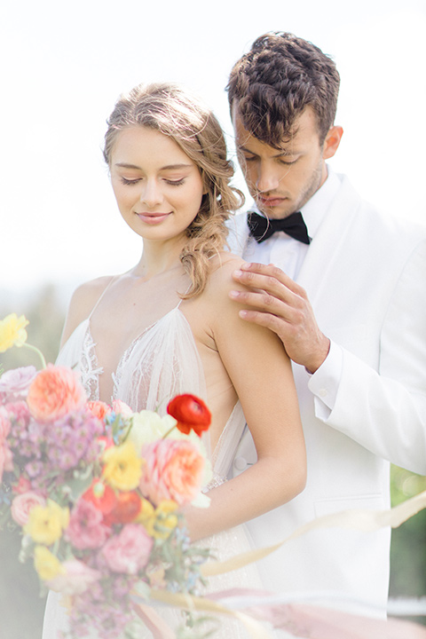  bride in a white flowing gown with a v neckline and the groom in a white dinner jacket and black pants 