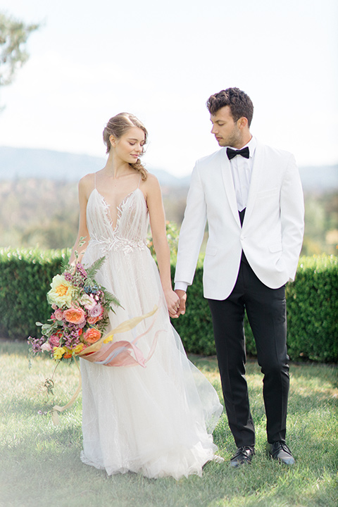  bride in a white flowing gown with a v neckline and the groom in a white dinner jacket and black pants 