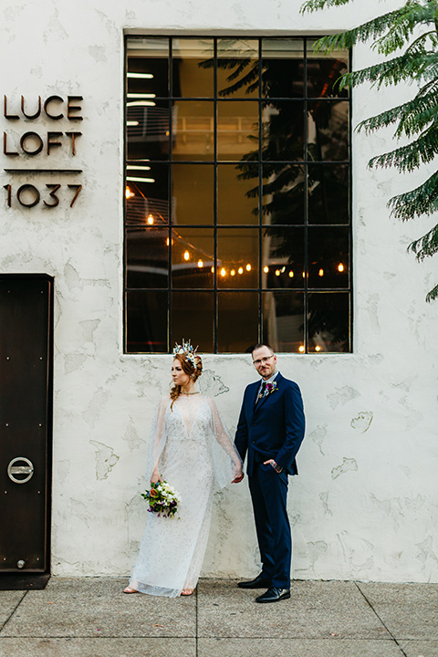  bride in an ivory lace gown with flowing sleeves and a braided hairstyle and the groom in a cobalt blue suit and a black long tie walking outside