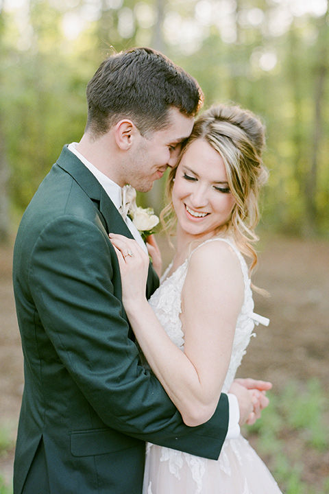  groom in a green suit with a grey bow tie and the bride in an ivory lace gown with an illusion neck line, touching heads