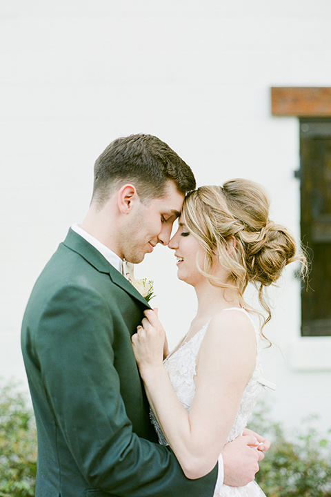  groom in a green suit with a grey bow tie and the bride in an ivory lace gown with an illusion neck line, embracing