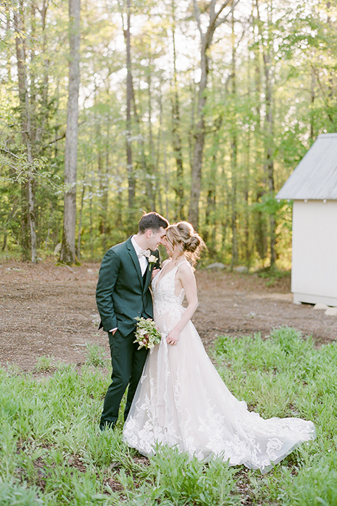  groom in a green suit with a grey bow tie and the bride in an ivory lace gown with an illusion neck line, touching heads