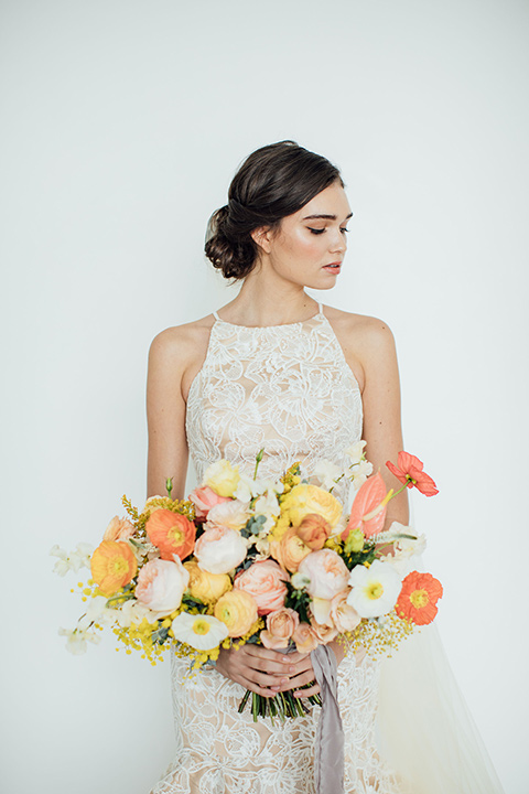  bride in a modern gown with a high neckline, no sleeves, and a tiered ruffled skirt 