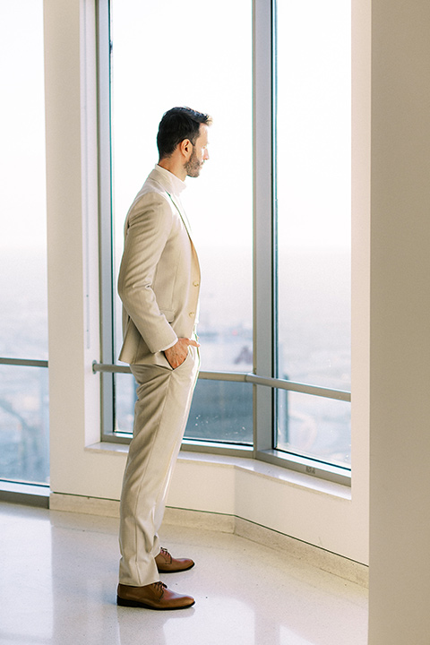 the groom in a light tan suit with a white shirt looking out the window