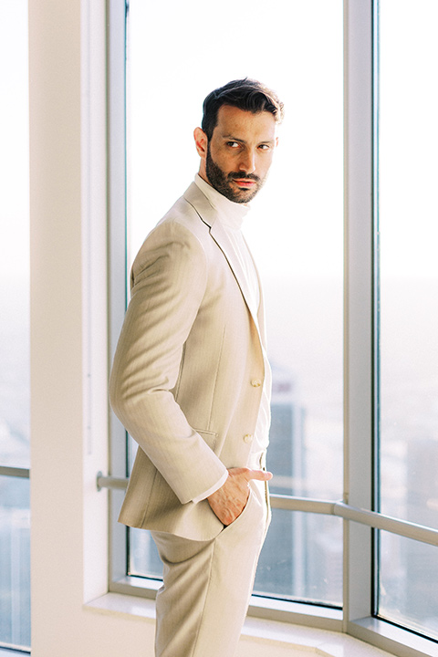 the groom in a light tan suit with a white shirt looking outside at the city