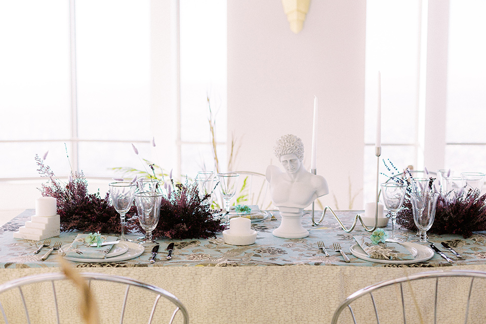  silver and blue floral tablecloth with white plates and silver flatware in front of windows overlooking the city