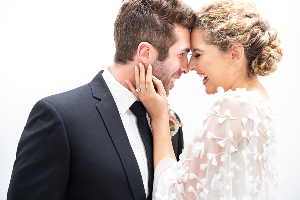  the bride in a lace white gown with long sleeves and a flowing skirt with hair in a modern low bun and the groom in a black suit with a long black tie 