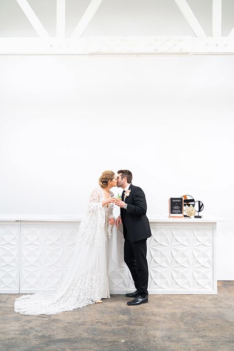  the bride in a lace white gown with long sleeves and a flowing skirt with hair in a modern low bun and the groom in a black suit with a long black tie 