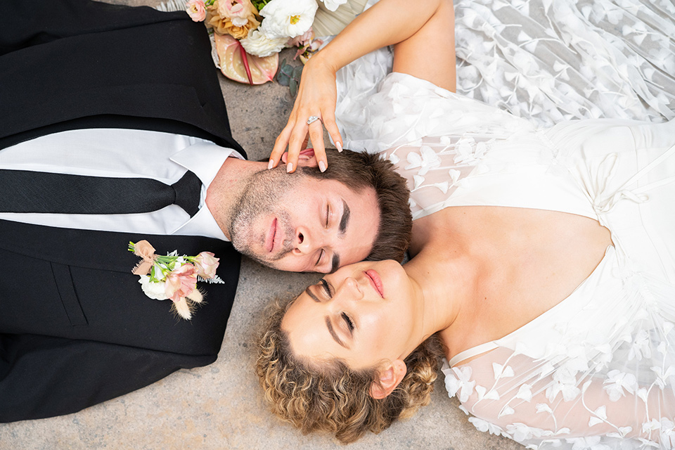  the bride in a lace white gown with long sleeves and a flowing skirt with hair in a modern low bun and the groom in a black suit with a long black tie 