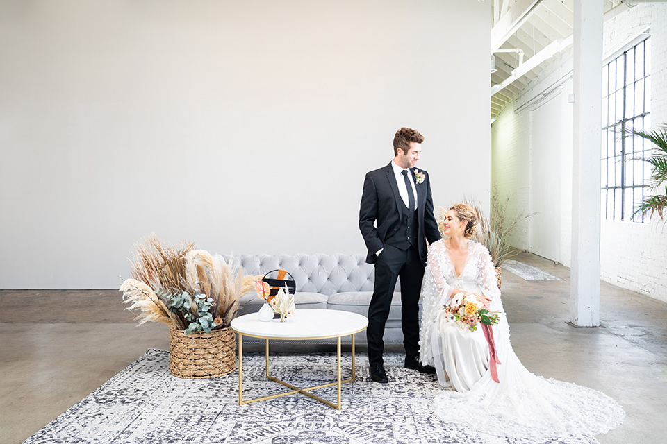  the bride in a lace white gown with long sleeves and a flowing skirt with hair in a modern low bun and the groom in a black suit with a long black tie 