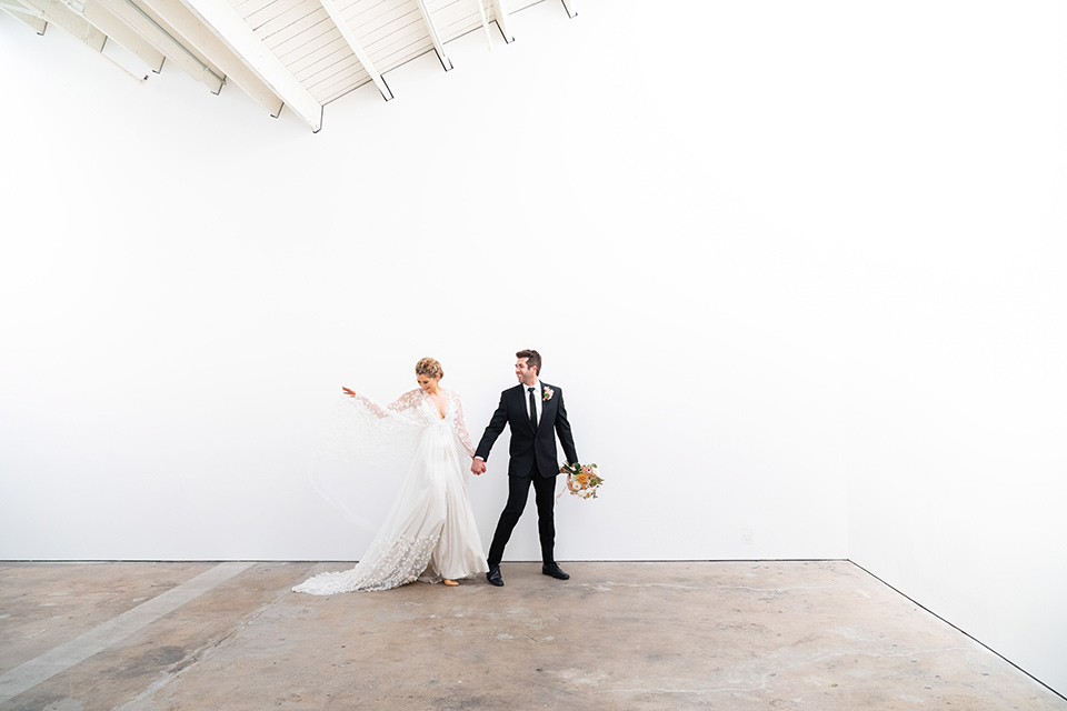  the bride in a lace white gown with long sleeves and a flowing skirt with hair in a modern low bun and the groom in a black suit with a long black tie 