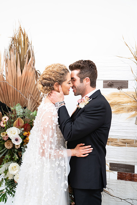  the bride in a lace white gown with long sleeves and a flowing skirt with hair in a modern low bun and the groom in a black suit with a long black tie 